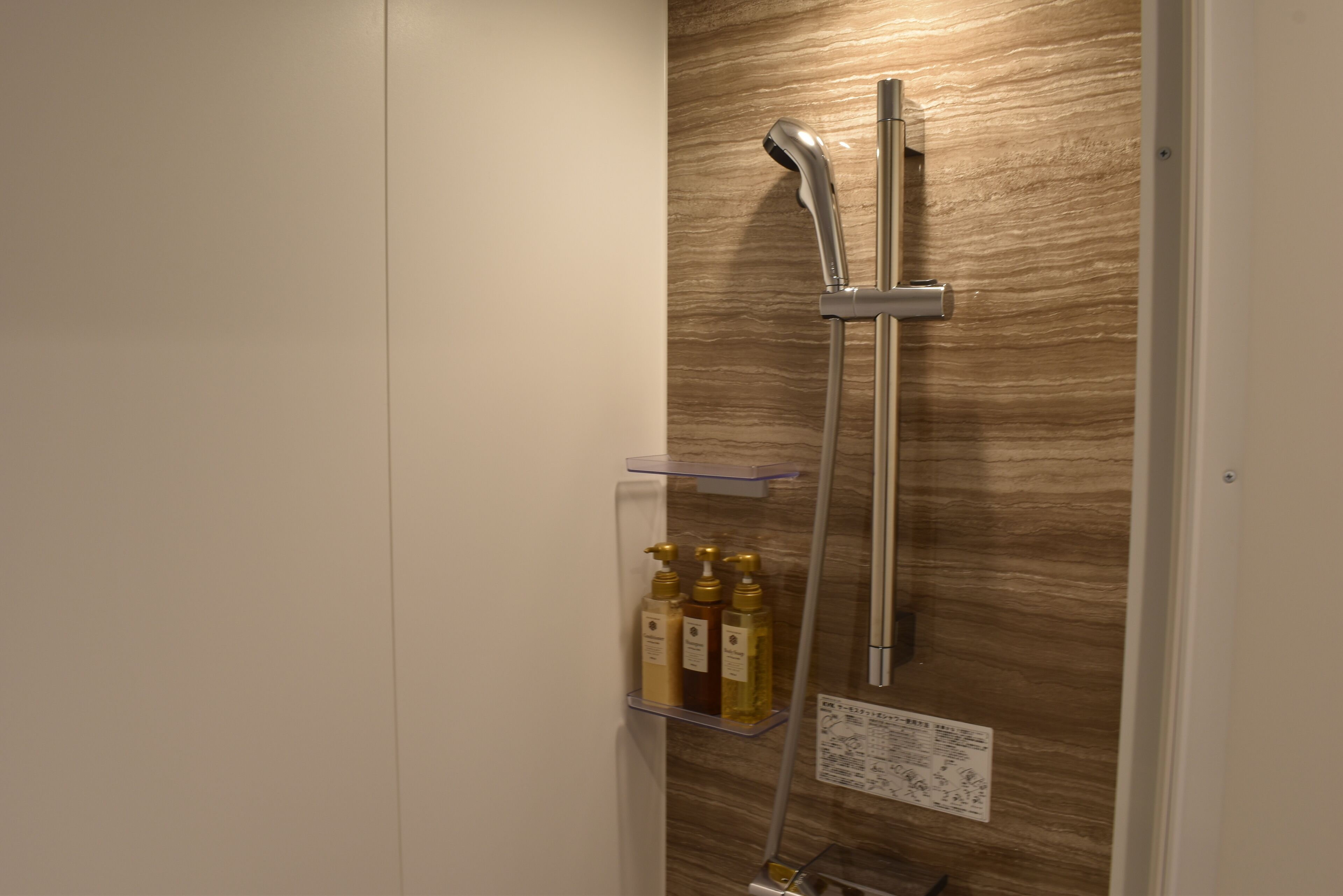 Una ducha con pared de madera, un estante con botellas y un cartel.