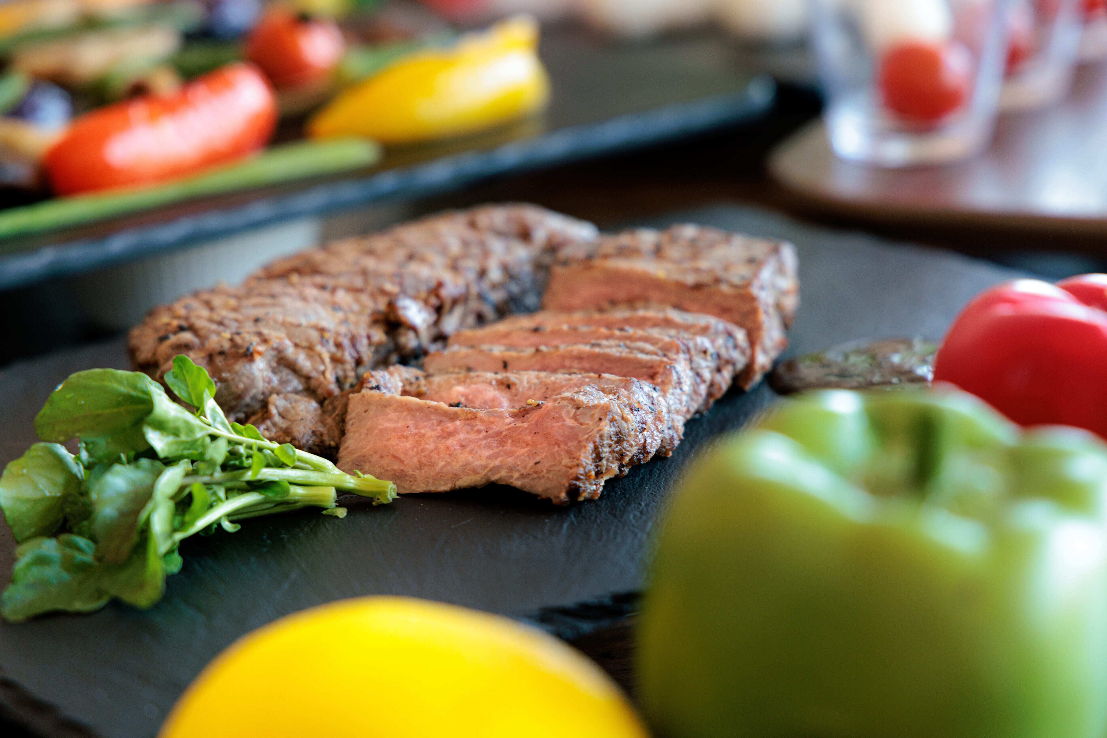 A steak with greens and a lemon on a slate board.