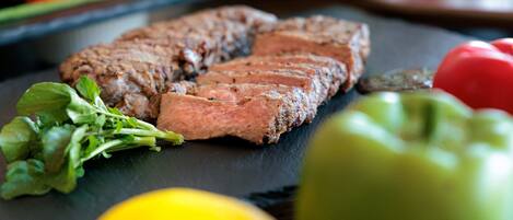 Un bistec con vegetales verdes y un limón sobre una tabla de pizarra.