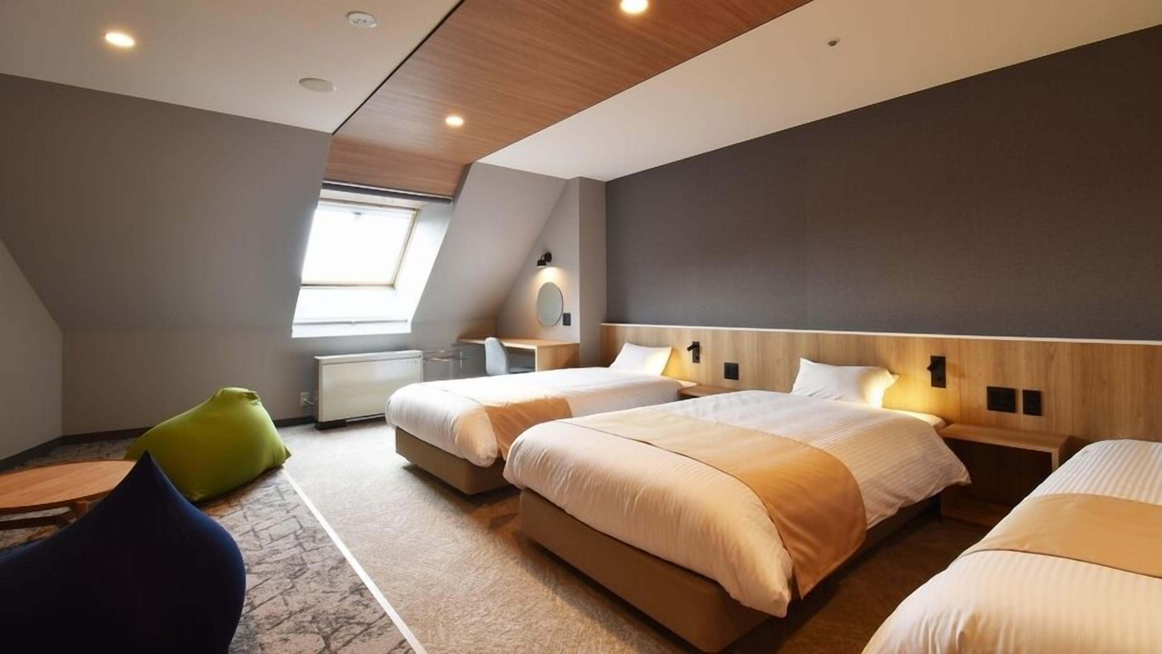 Een moderne hotelkamer met twee bedden, een bureau, een stoel en een dakraam.