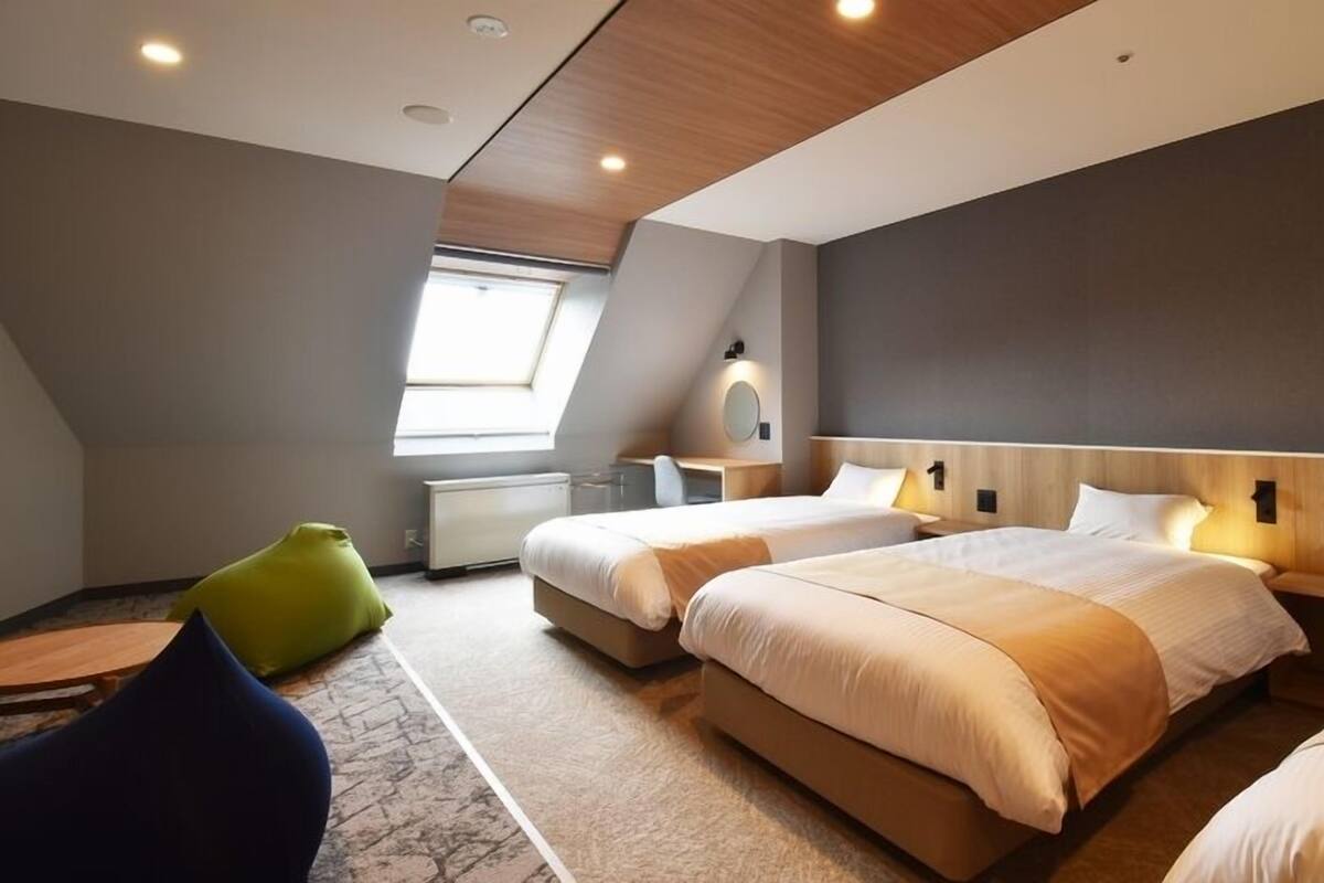 Una habitación de hotel moderna con dos camas, un escritorio, una silla y un tragaluz.