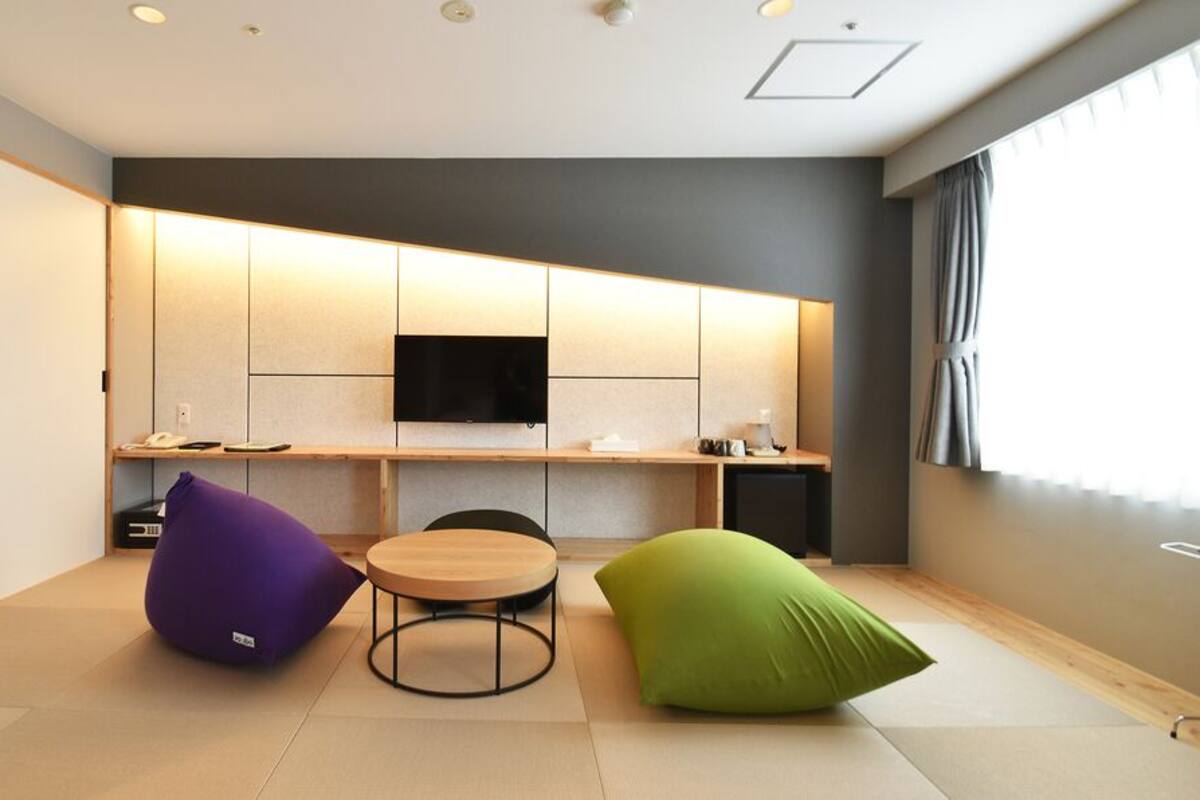 Una habitación moderna con televisión de pantalla plana, una mesa redonda y dos sillones de mimbre.