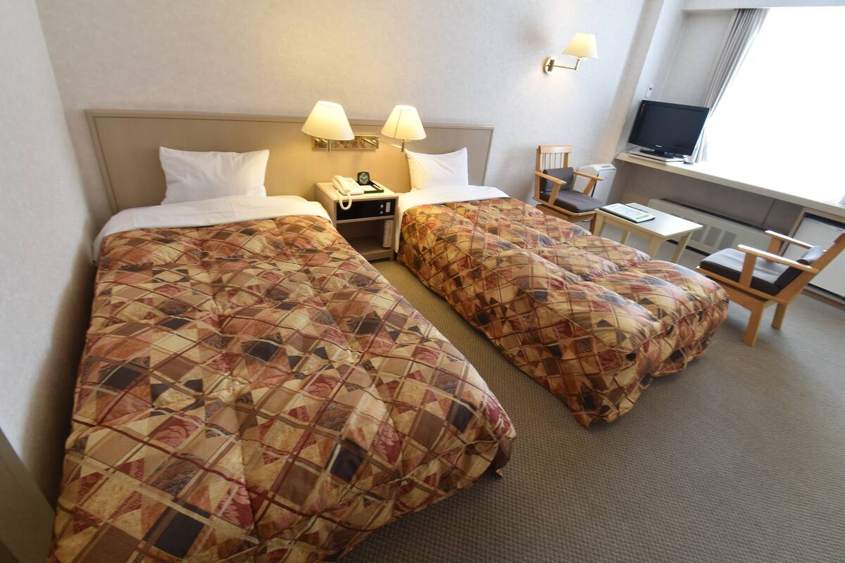 Una habitación de hotel con dos camas, un escritorio, un televisor y una silla.