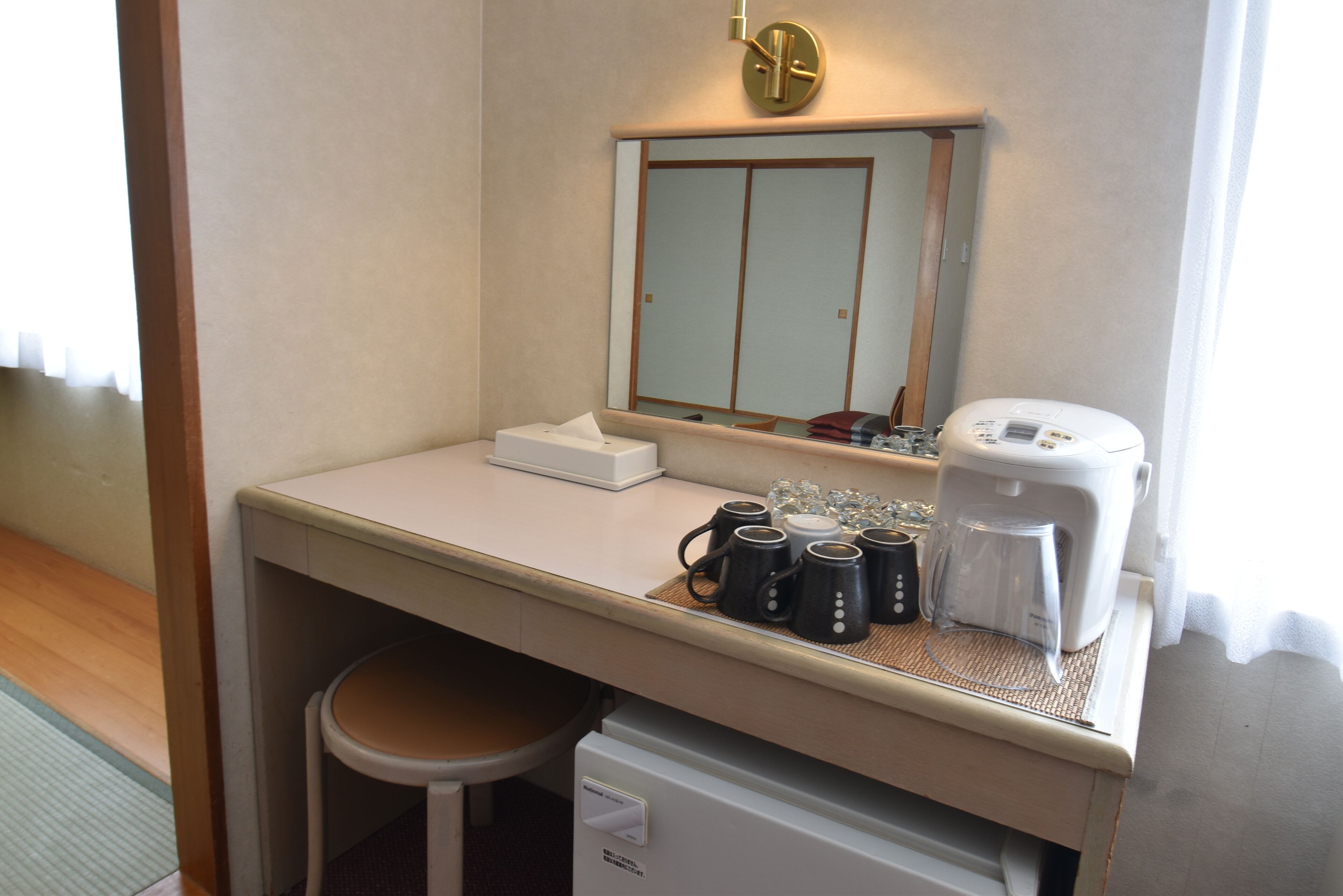A hotel room with a kitchenette area, including a coffee maker, mugs, and a small refrigerator.