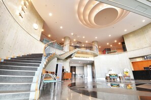 Un vestíbulo amplio con una escalera central, una recepción y un diseño de techo moderno.