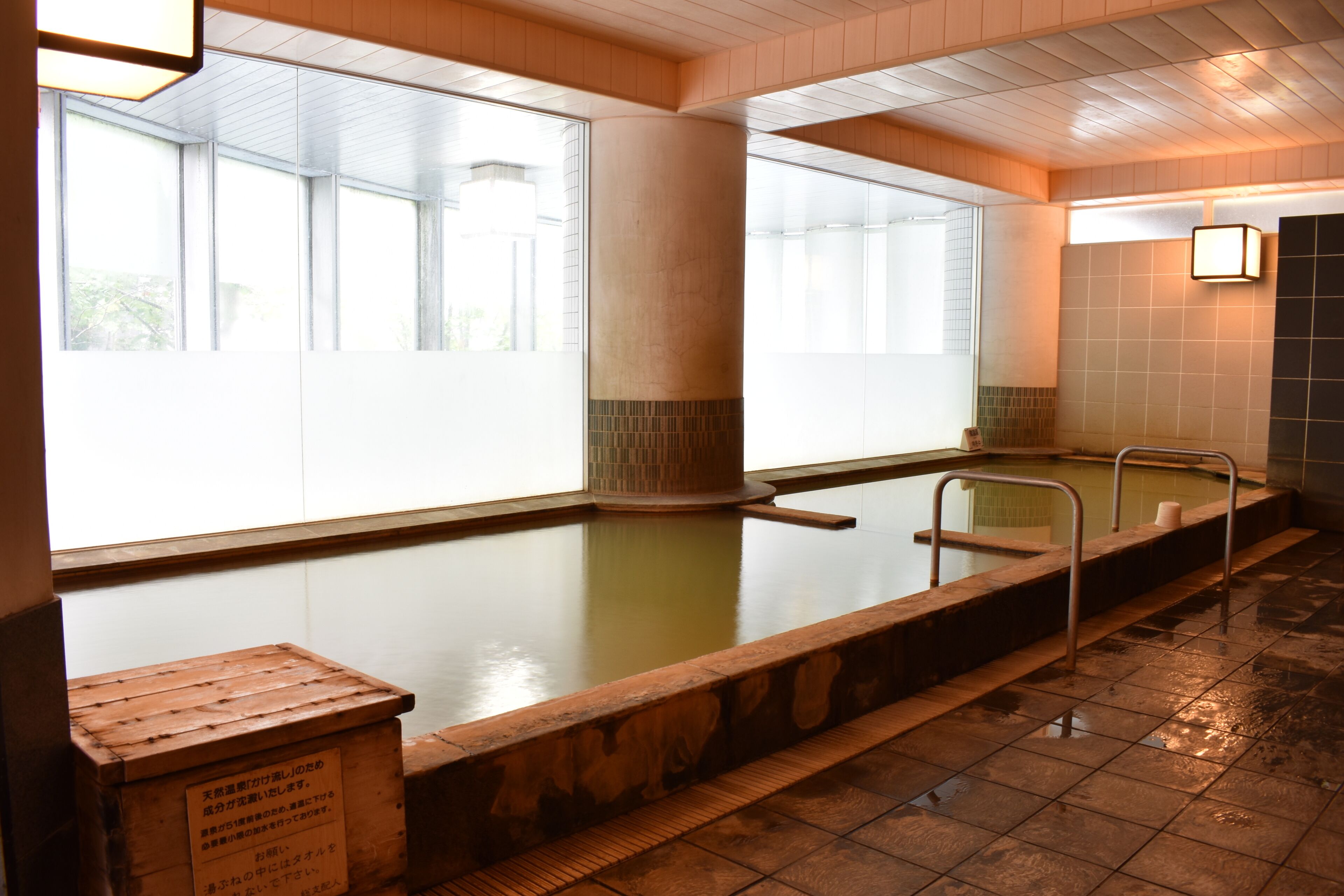 Una amplia piscina cubierta con paredes de vidrio transparente, un banco de madera y suelo de baldosas.
