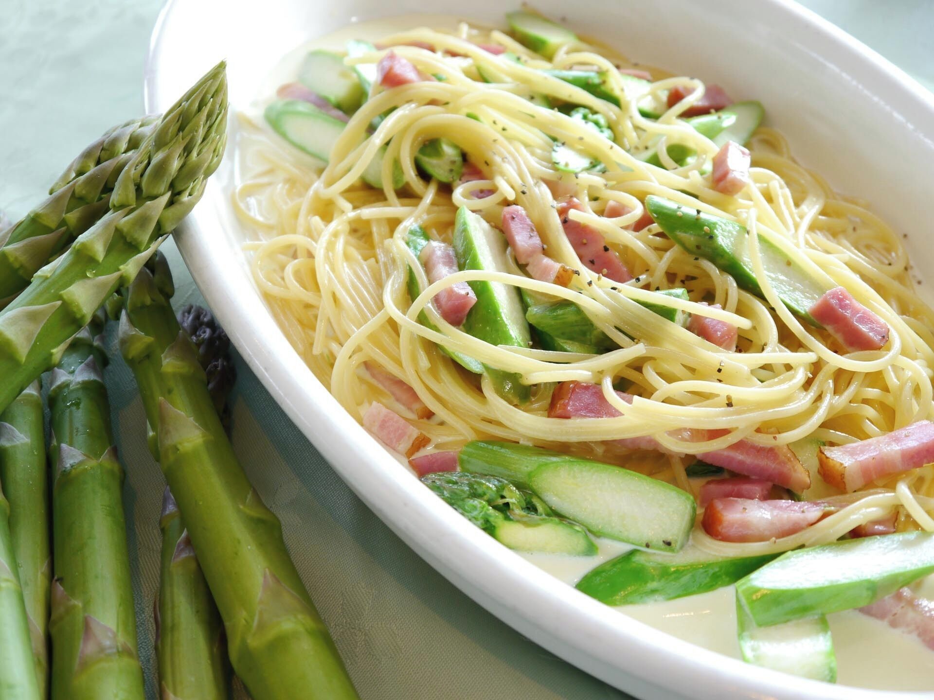 Un plato de espagueti con espárragos, pepino y jamón.