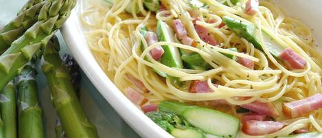 Un plato de espagueti con espárragos, pepino y jamón.