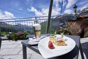 A dessert plate with a slice of cake, a strawberry, and a glass of beer on a table with a mountain view in the background. - Alpenhotel Laurin (Soelden)