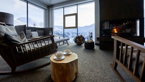 A cozy room with a large window, a fireplace, a wooden rocking chair, and a small round table with a teapot and cups. - Alpenhotel Laurin (Soelden)