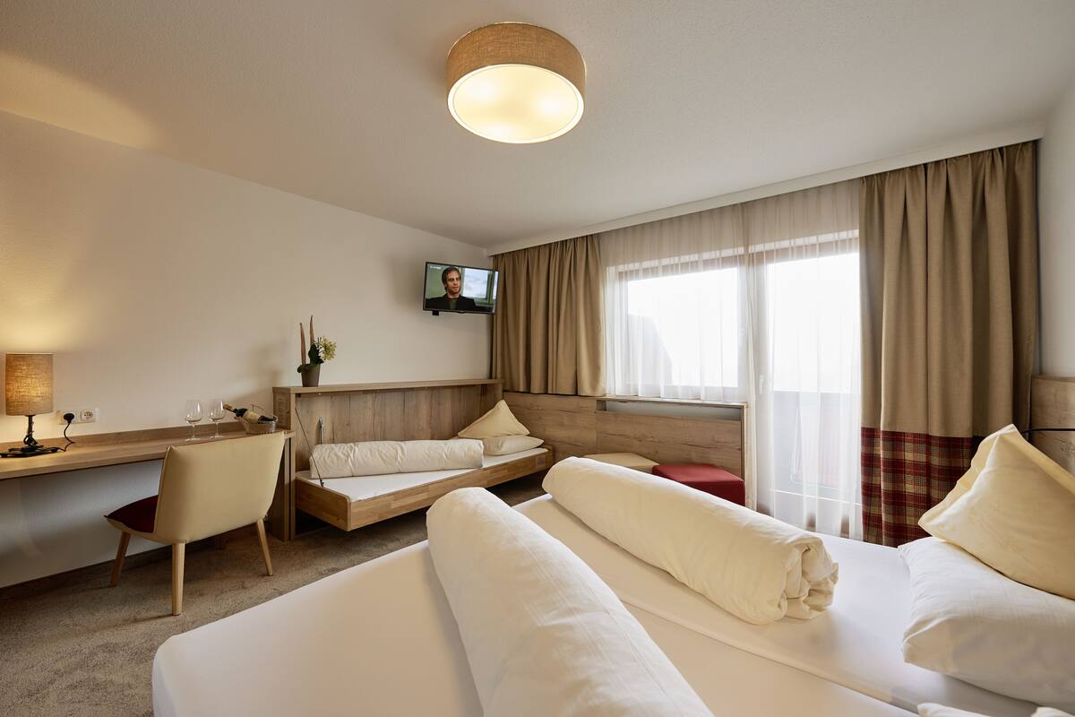 A hotel room with a bed, a desk with a chair, a television, and a window with curtains.