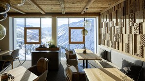 A modern interior with wooden ceiling beams, large windows with mountain views, and a wall decorated with carved wooden panels. - Alpenhotel Laurin (Soelden)