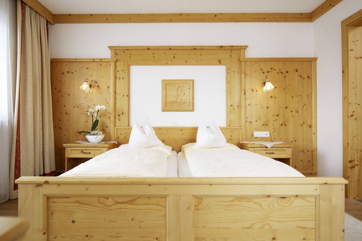 A double bed with wooden headboard and footboard, two bedside tables with lamps, a potted plant, and a framed picture on the wall.
