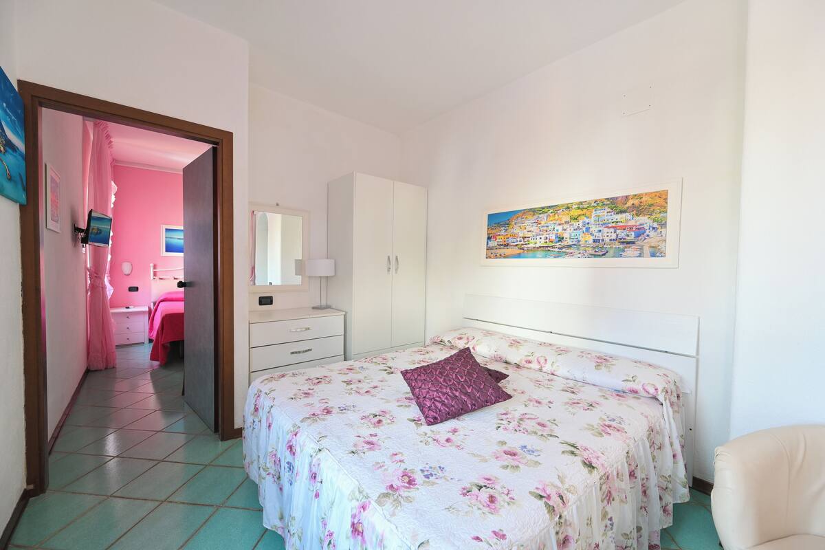 A bedroom with a bed, a wardrobe, a desk, a chair, and a painting on the wall.