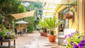 Un área de patio al aire libre con muebles de mimbre, plantas en macetas y fachada de edificio amarilla.