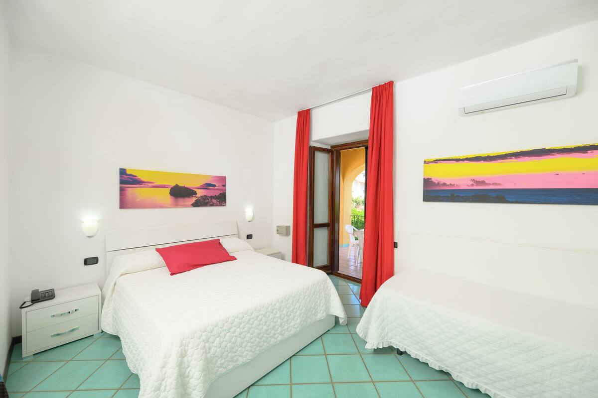 A bedroom with a bed, a nightstand, a red curtain, and two paintings on the walls.