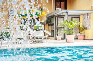 A swimming pool area with lounge chairs and umbrellas, a covered seating area, and potted plants. - Hotel Annabelle (Ischia)