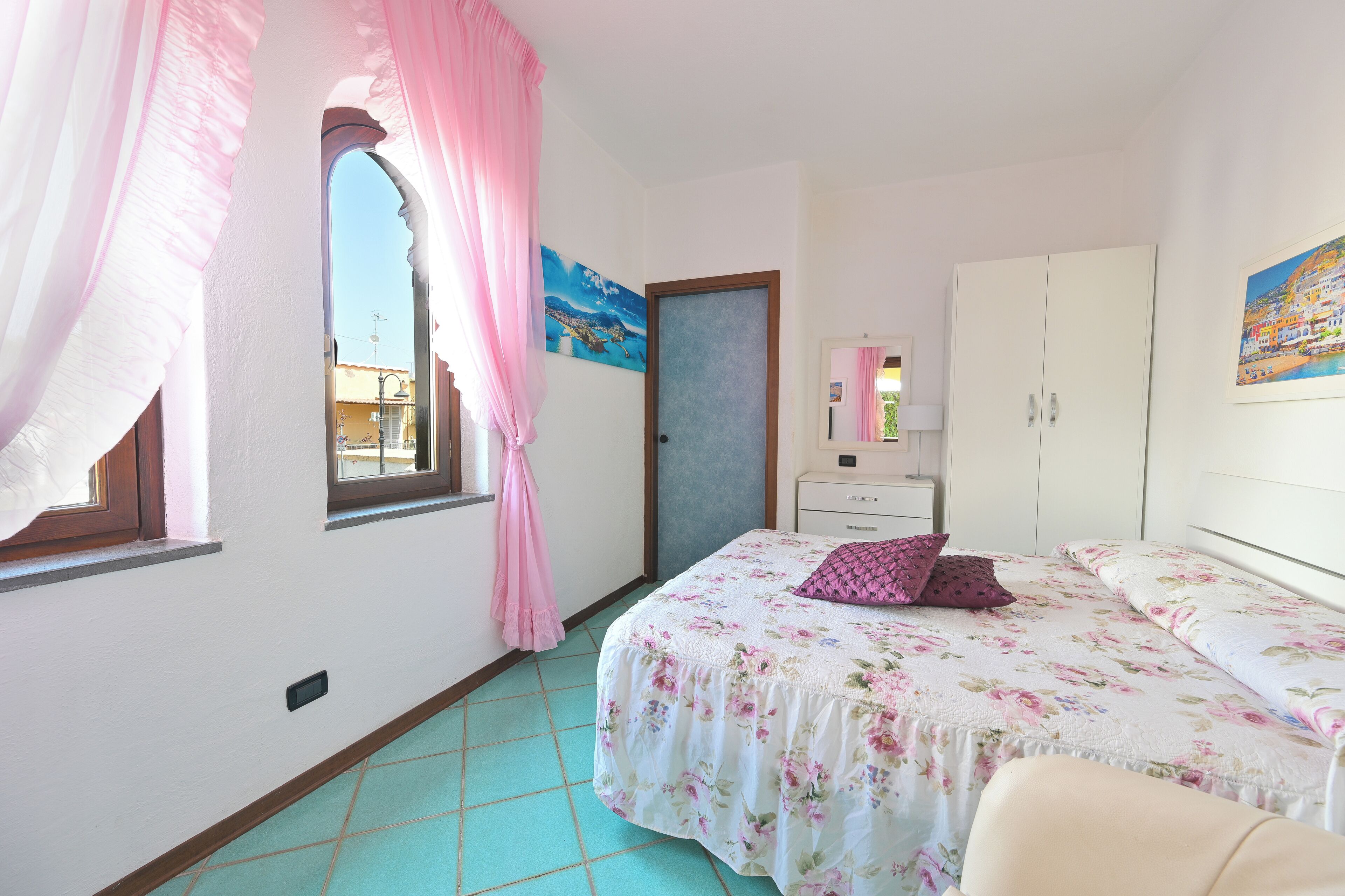 A bedroom with a bed, a wardrobe, a window with curtains, and a painting on the wall.