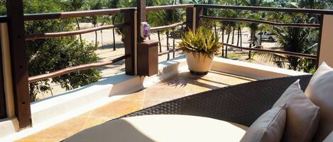 A balcony with a view of the beach, a potted plant, and a cushioned seating area.