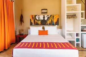 Habitación de hotel con una cama grande, cortinas naranjas, un cuadro sobre la cama y una estantería blanca a la derecha.