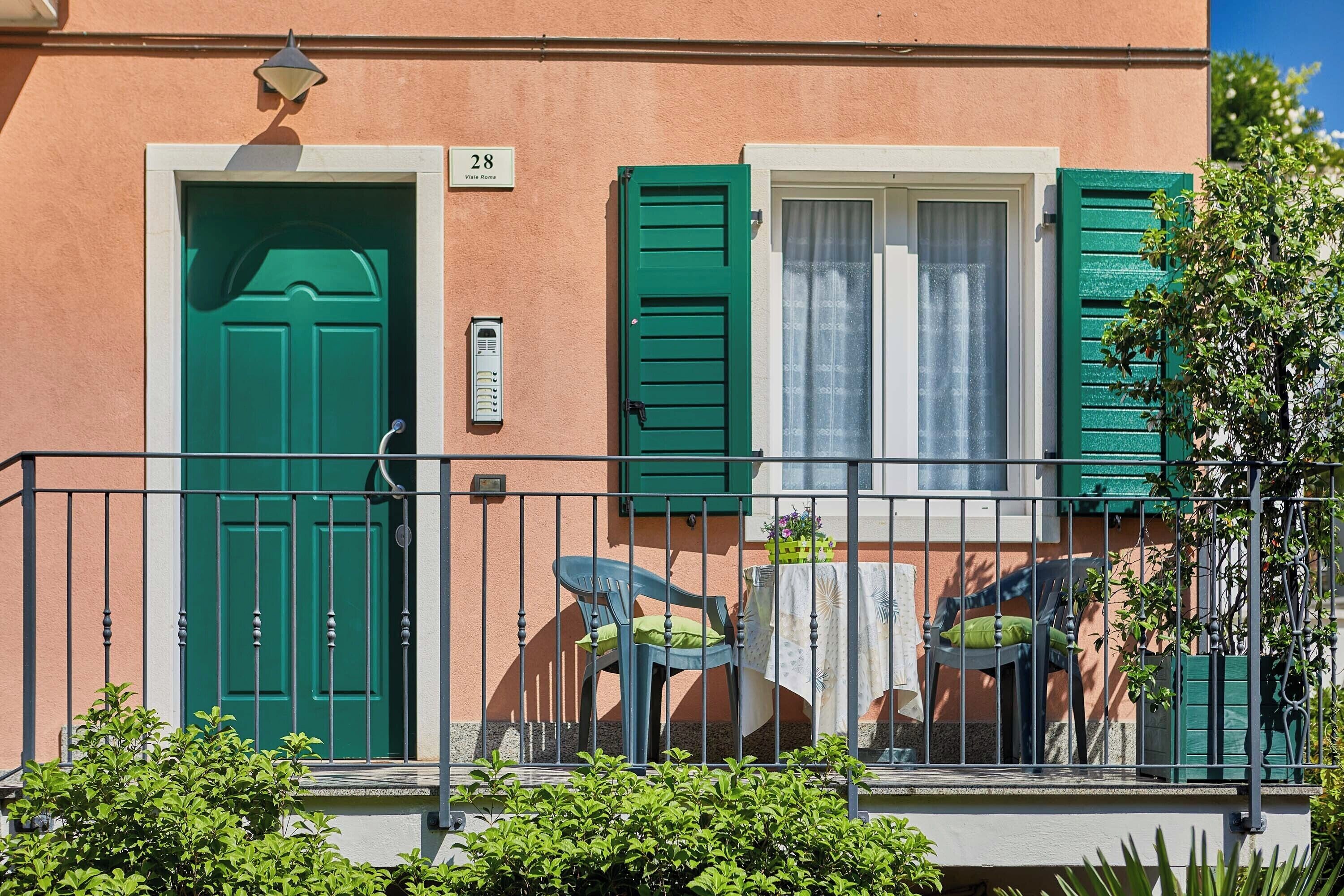 A building with a green door, a window with green shutters, and a balcony with chairs and a table.