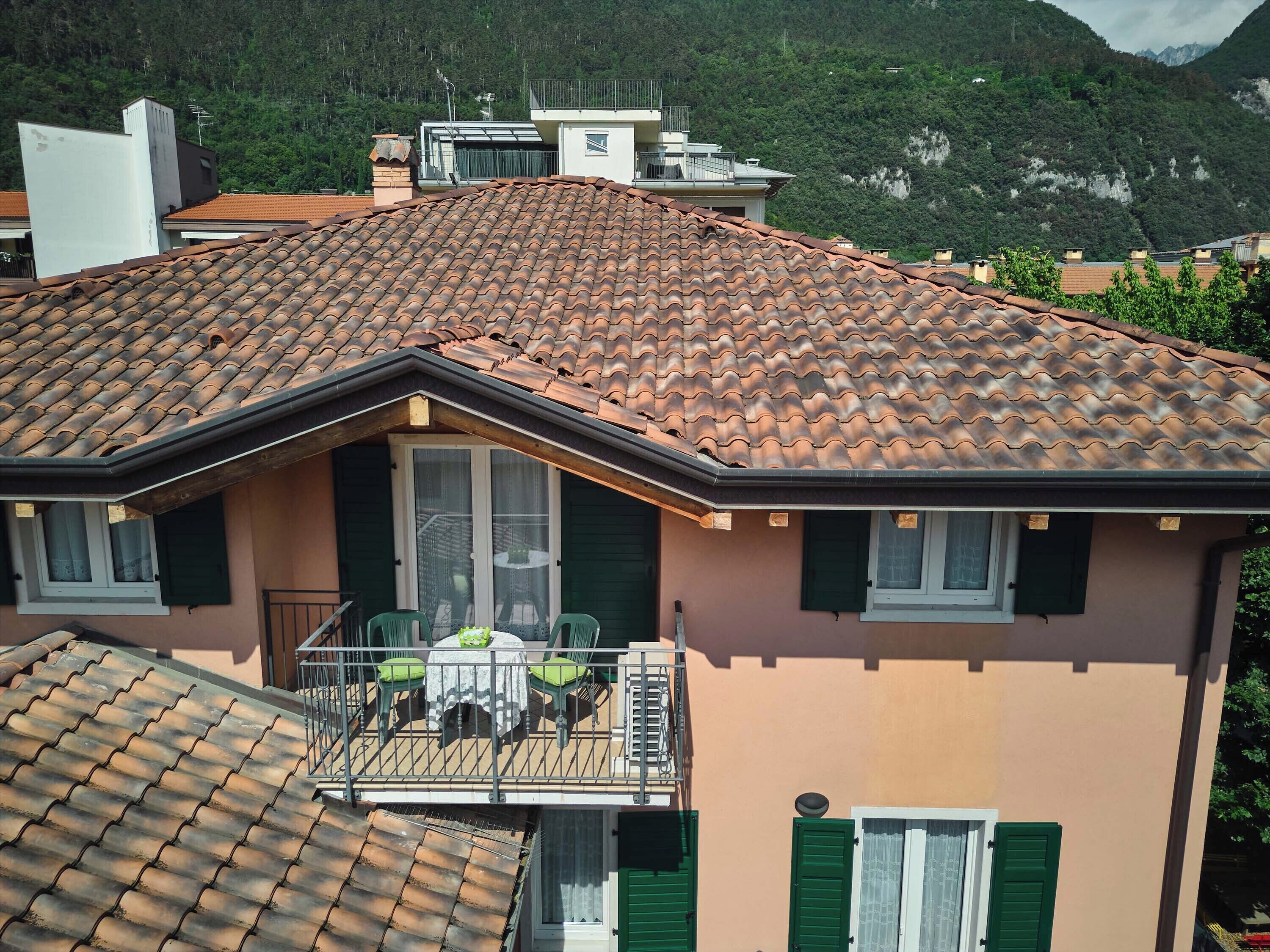 Un bâtiment à deux étages, doté d’un toit recouvert de tuiles, d’un balcon avec une table et des chaises, et offrant une vue sur un paysage montagneux.