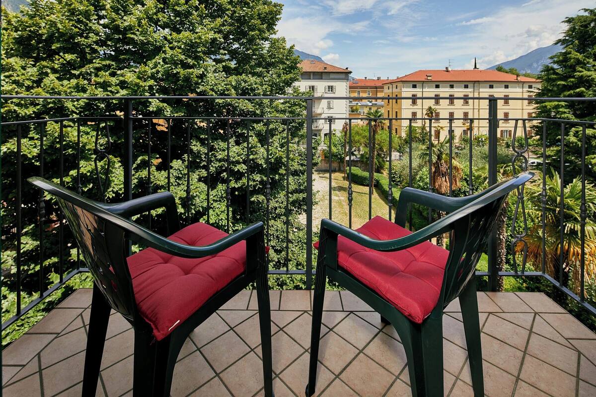 Two chairs with red cushions on a balcony with a view of buildings and trees.