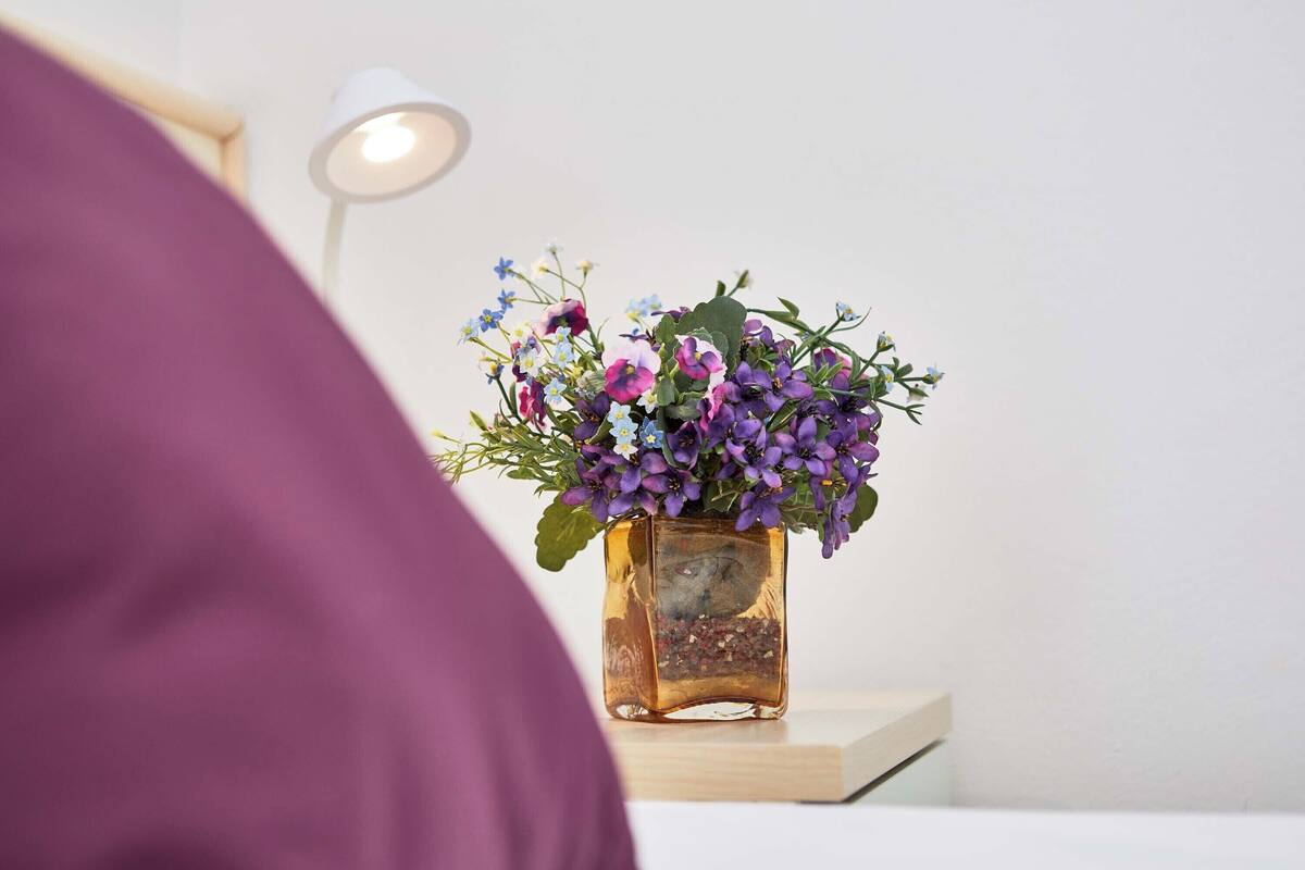 A square glass vase with purple and blue flowers on a bedside table.
