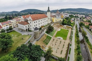 Vista aérea de un pueblo histórico con un castillo destacado, una iglesia y una plaza pública bien cuidada con una fuente.