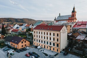 Un hotel con techo rojo y una torre de reloj, rodeado de otros edificios y un paisaje montañoso al fondo.