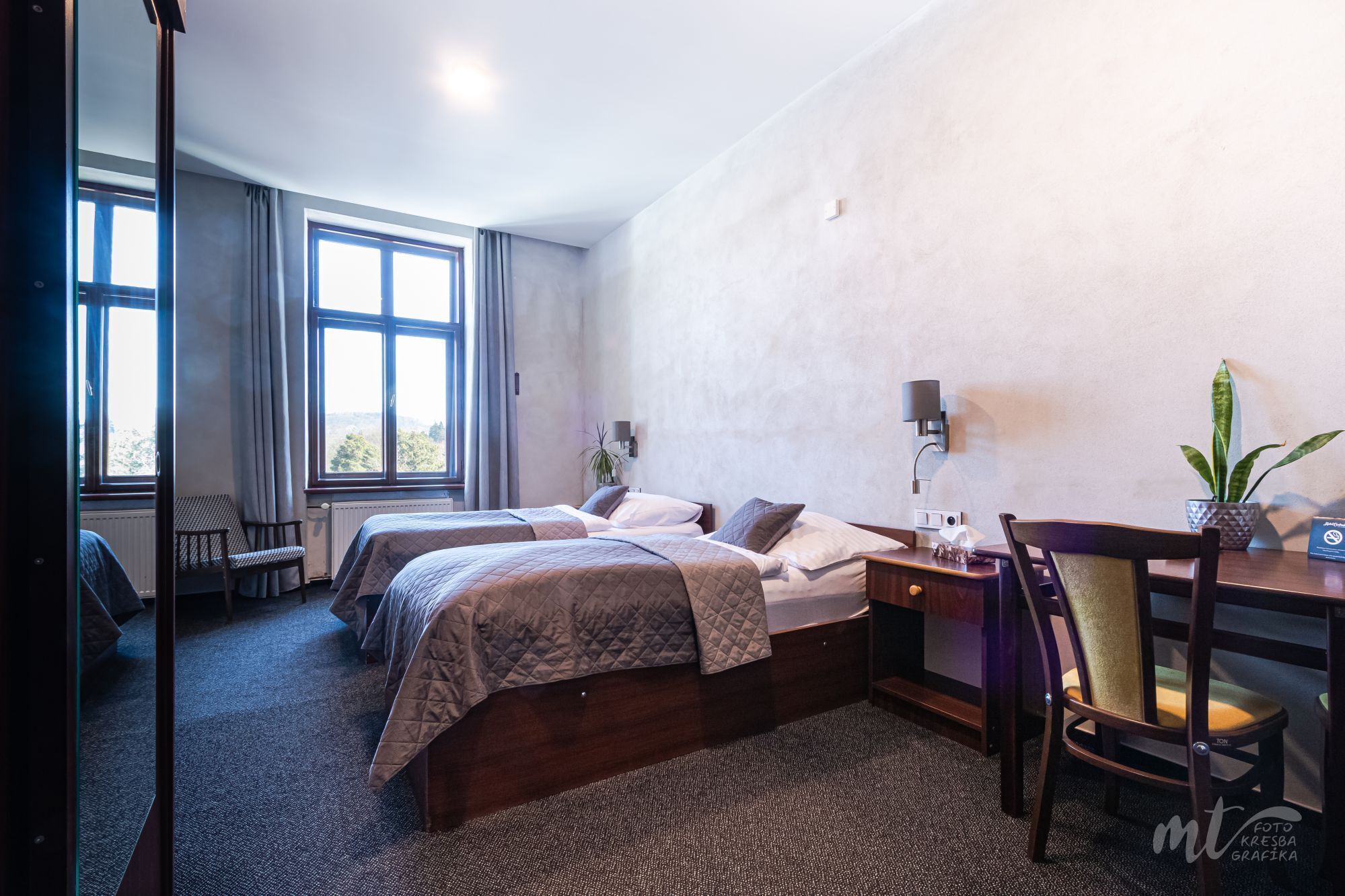 Habitación de hotel con dos camas, un escritorio con silla, una lámpara y una planta.