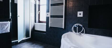 A modern bathroom with a bathtub, a towel rack, and a window with blinds.