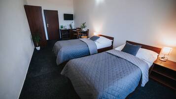 A hotel room with two beds, a desk, a chair, and a TV on the wall.