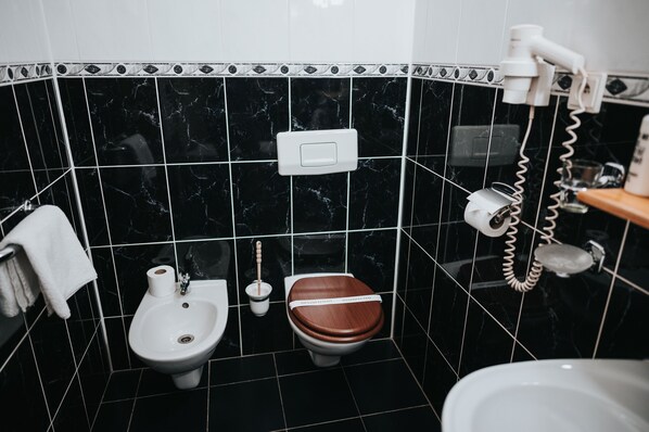 A bathroom with black marble tiles, a white bidet, a wooden toilet seat, and a white towel hanging on the wall.