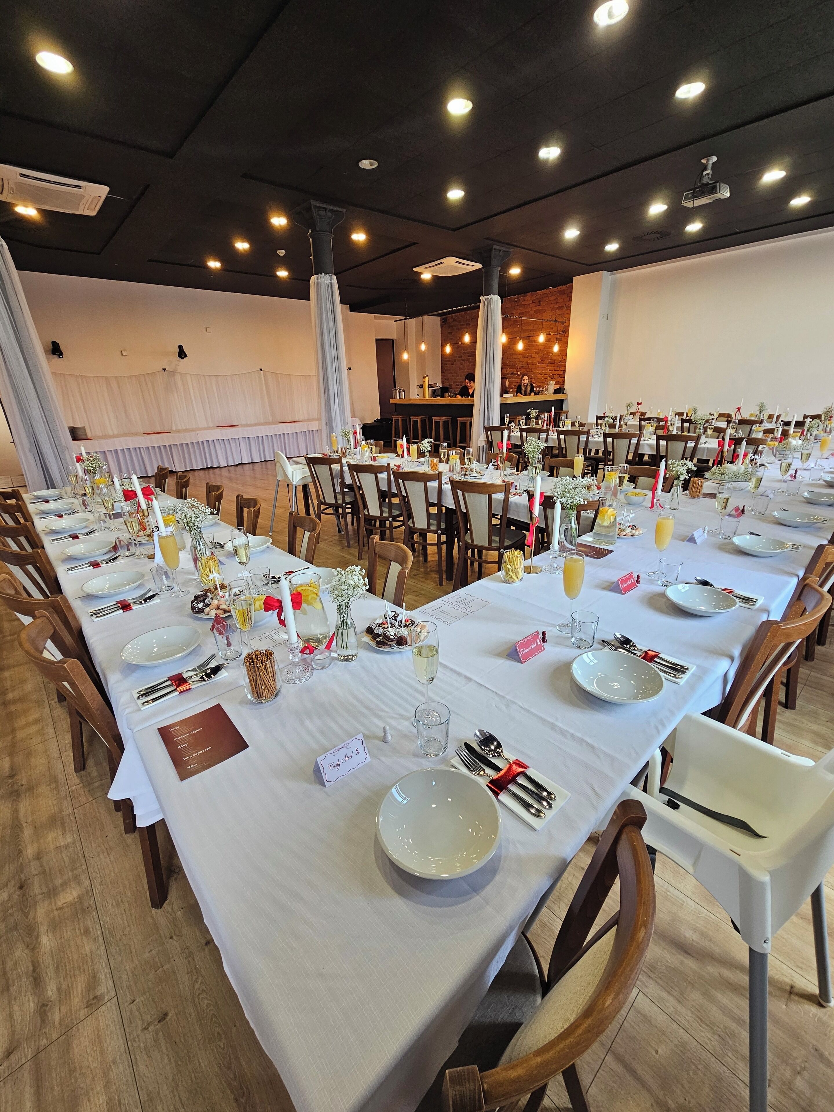 A banquet hall with long tables set for a formal event, featuring white tablecloths, neatly arranged place settings, and floral centerpieces.