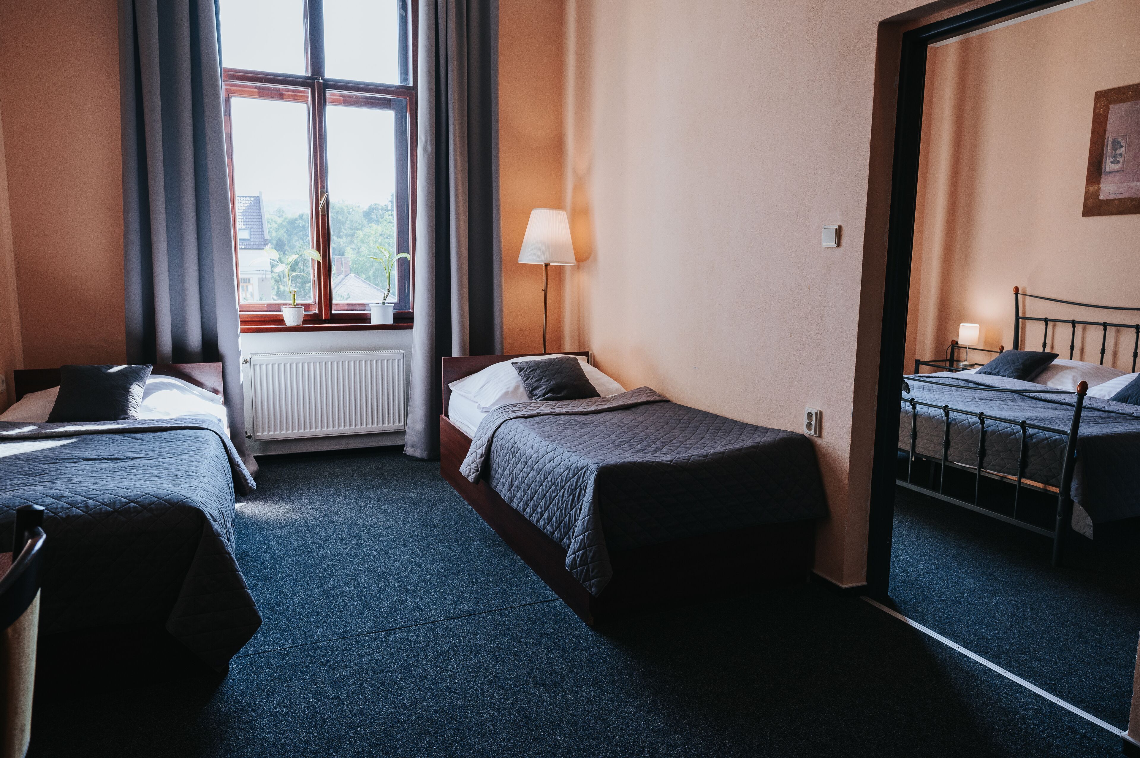 Une chambre d’hôtel avec deux lits simples, une fenêtre avec des rideaux, une lampe sur pied et un radiateur.