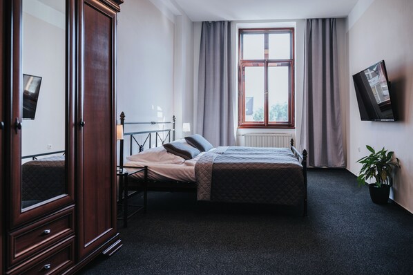 A bedroom with a bed, a wardrobe, a window with curtains, a radiator, a television, and a potted plant.