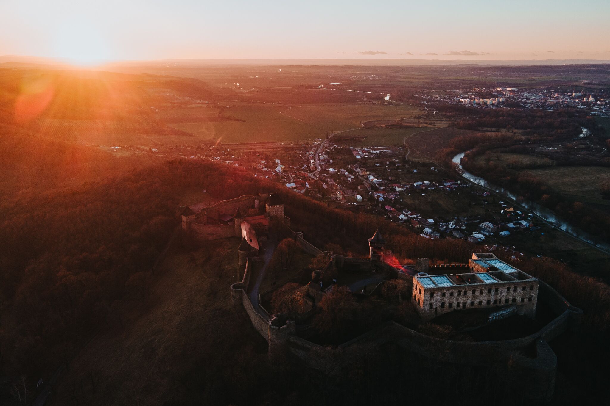 Luchtbeeld van een historische stad met een opvallende, kasteelachtige structuur, omringd door velden en een rivier.