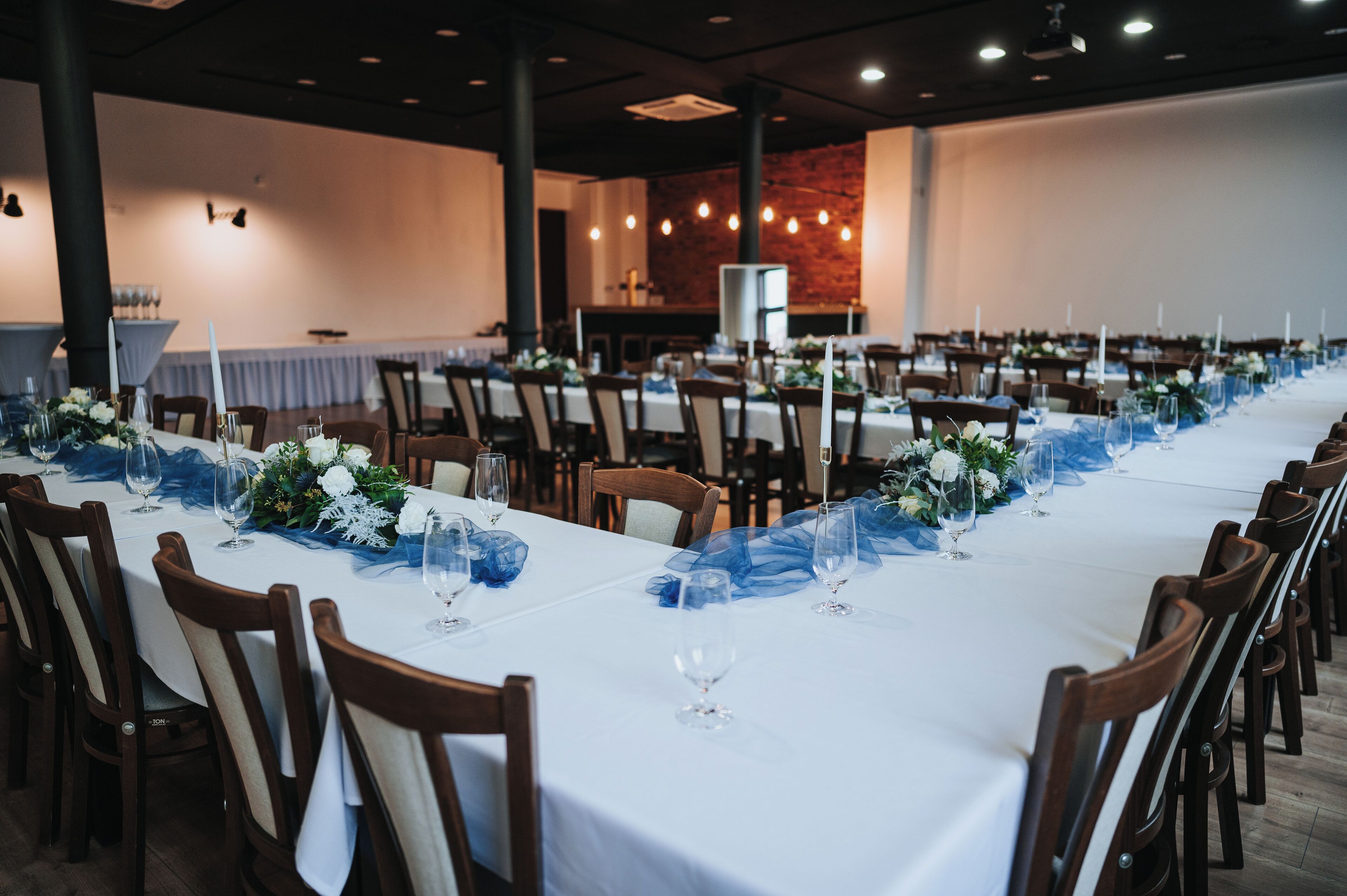 A long banquet table set with white tablecloths, blue drapes, and floral centerpieces.