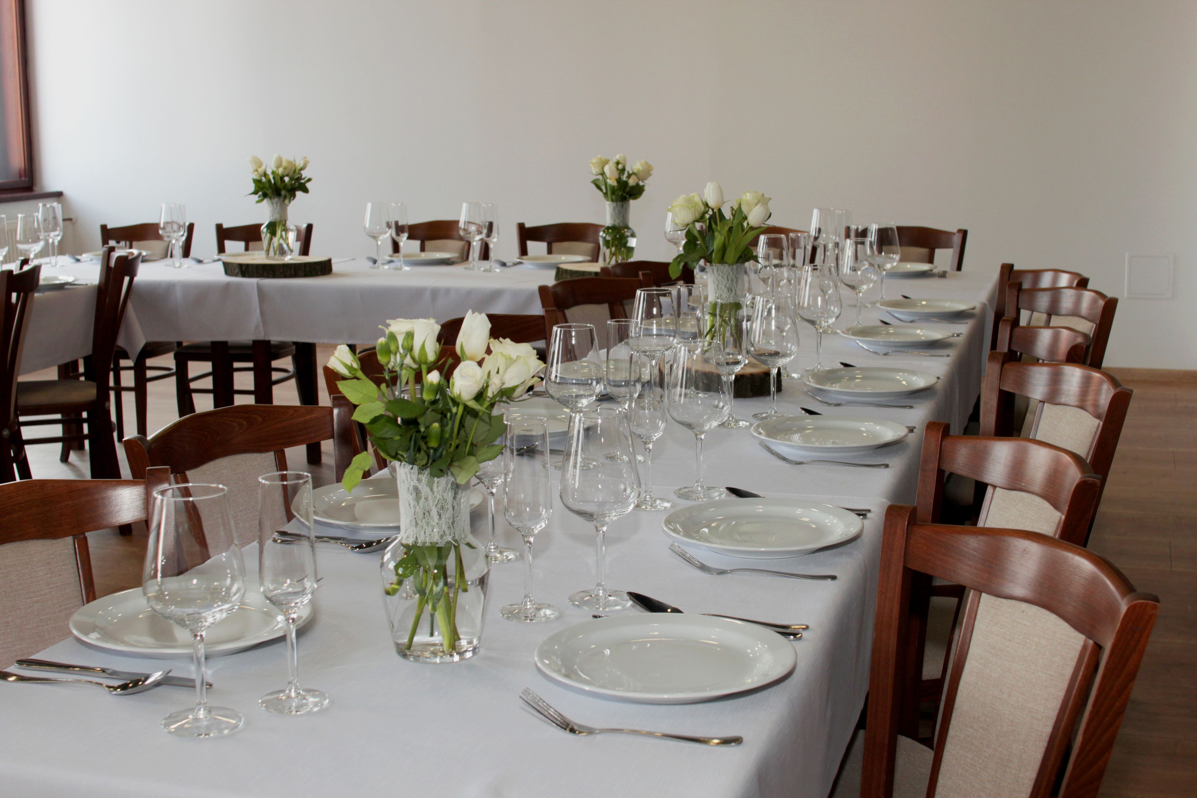 A long dining table set with white tablecloths, multiple sets of cutlery, and vases with flowers.