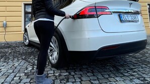 Um Tesla branco estacionado em frente a um edifício com uma placa que diz 'HOTEL'.