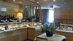 A wooden interior with a bar area displaying wine bottles and glasses, a dining table with a potted plant, and a kitchen area with dishes and utensils. - Hotel Pedretti (Branzi)