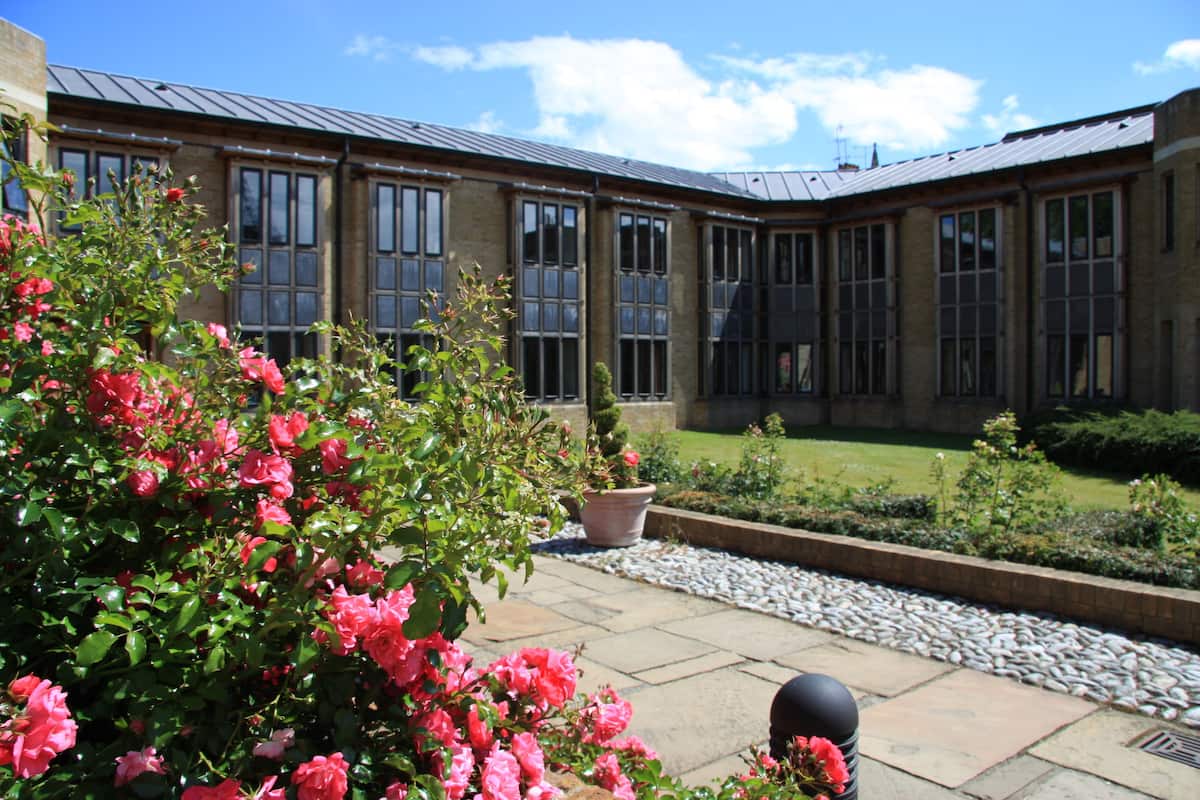A courtyard with a brick building, large windows, and a garden with pink flowers.