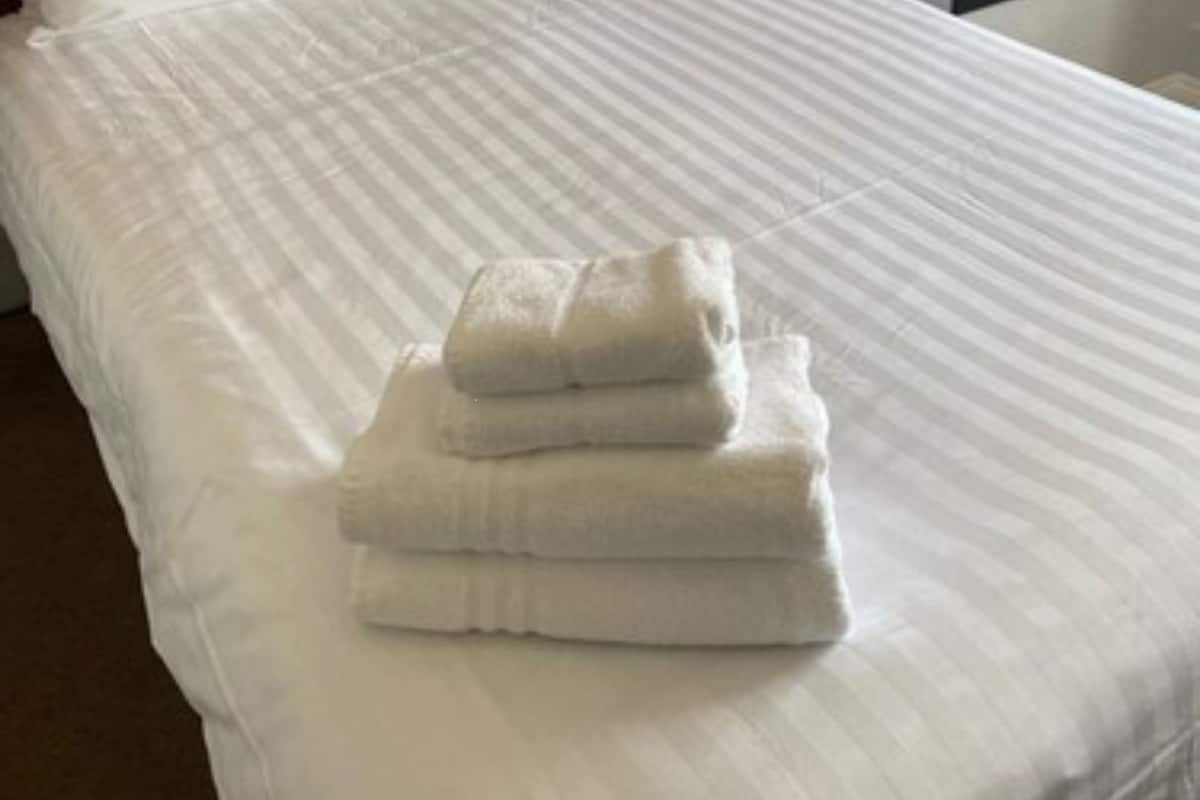 A neatly made bed with white linens and a folded towel on the bed.