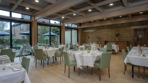 A restaurant with multiple tables set for dining, large windows, and a brick wall interior. - Canterbury Cathedral Lodge (Canterbury)