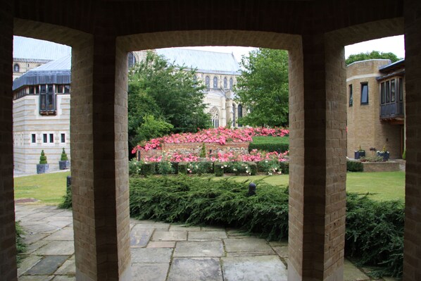 A stone archway framing a view of a historic building with a garden of pink flowers. - Canterbury Cathedral Lodge (Canterbury)
