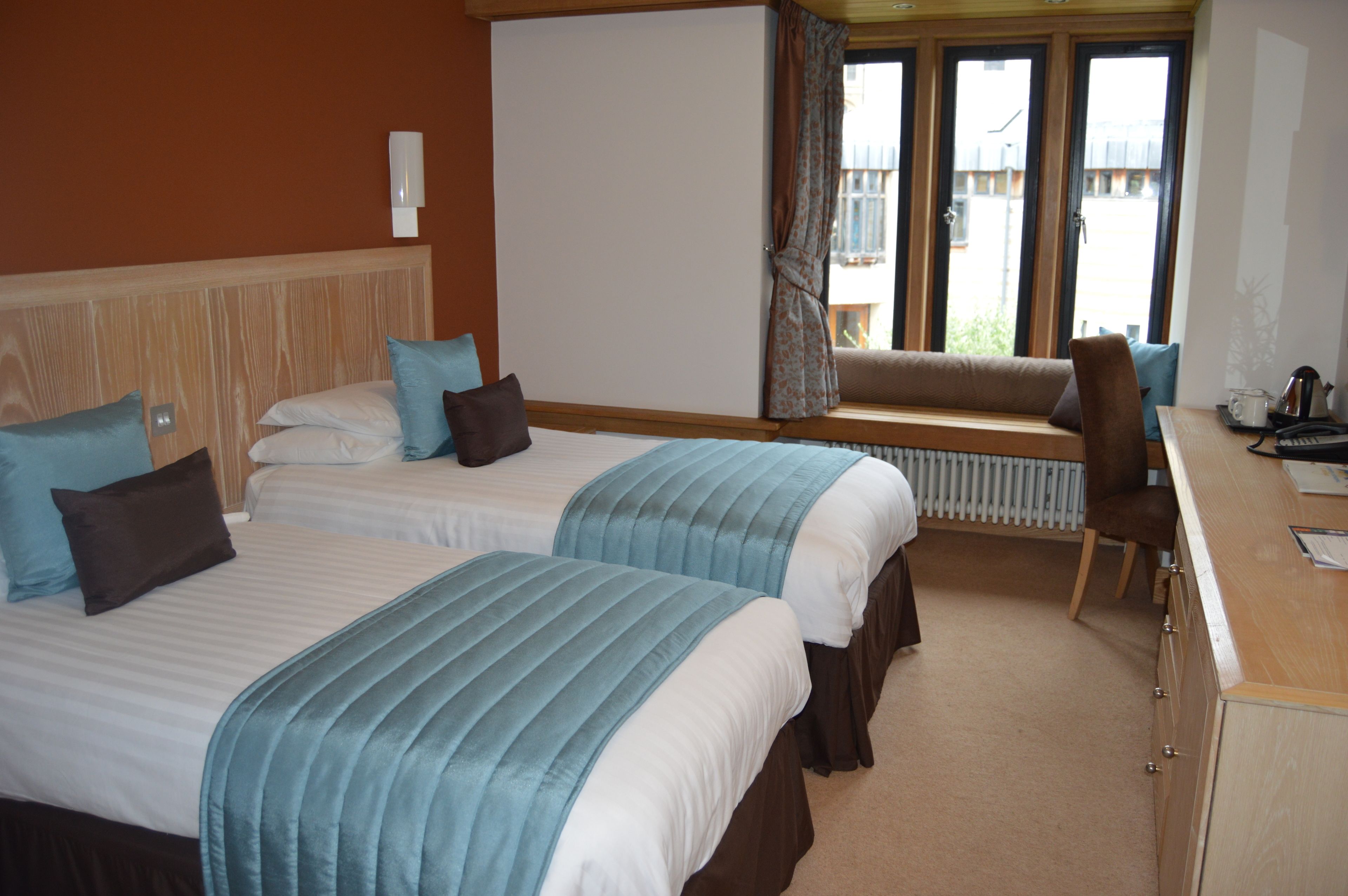 Une chambre d’hôtel avec deux lits, un bureau, une chaise, une fenêtre avec des rideaux et un radiateur.
