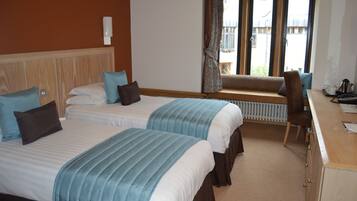 Une chambre d’hôtel avec deux lits, un bureau, une chaise, une fenêtre avec des rideaux et un radiateur.