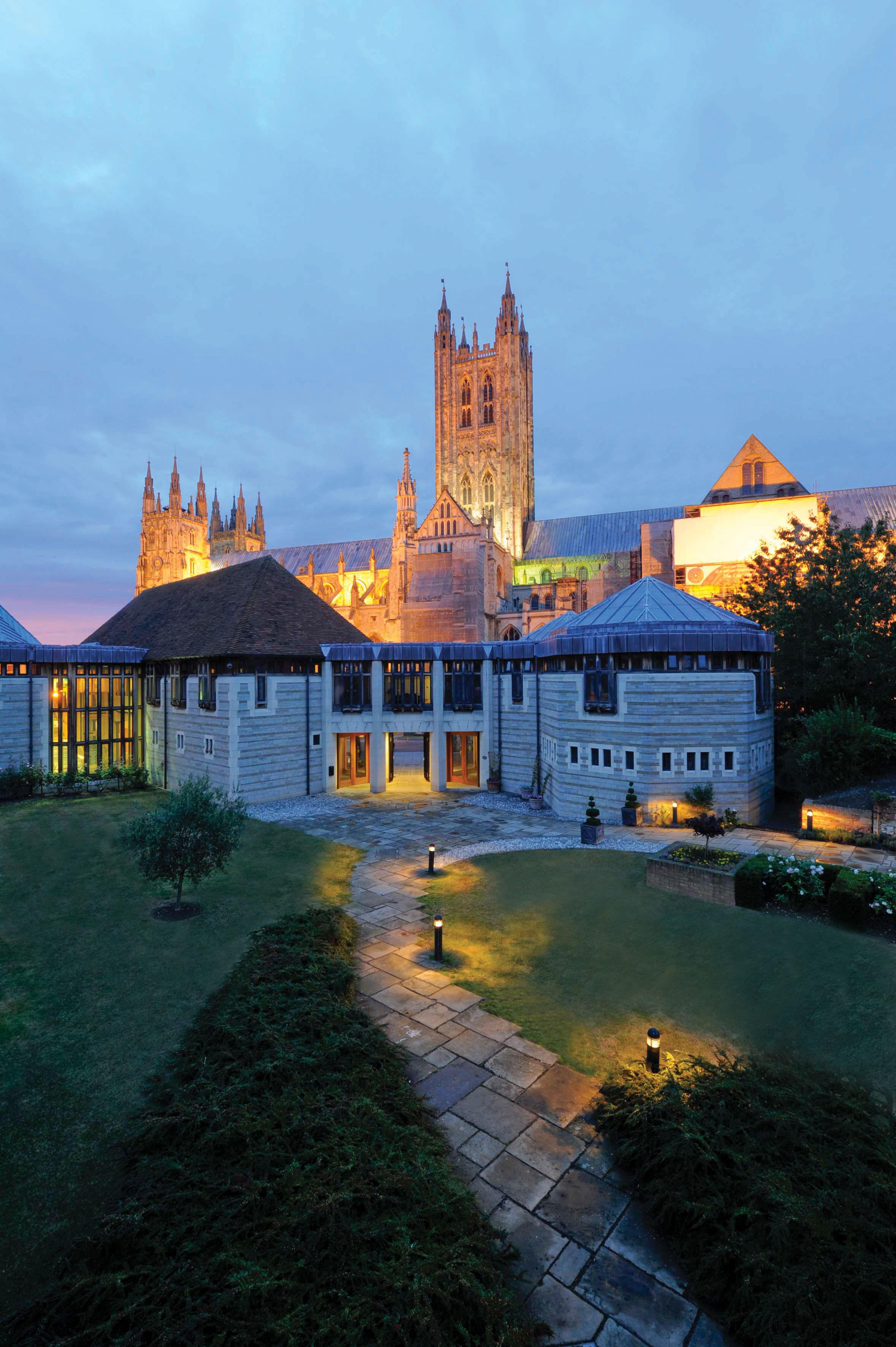 A historic building with a prominent tower and a courtyard with a pathway leading to a small pond.