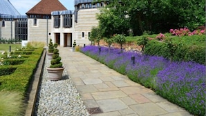 A building with a central entrance, surrounded by a garden with purple flowers and neatly trimmed hedges. - Canterbury Cathedral Lodge (Canterbury)